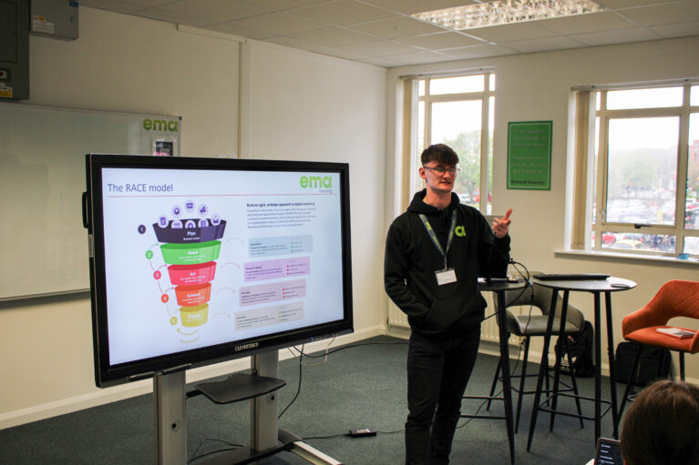 Marketing trainer stood presenting next to digital board